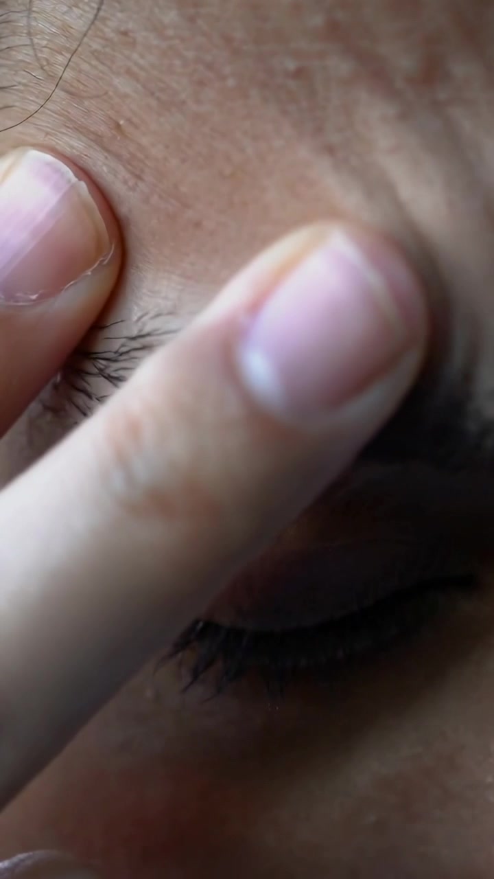 Vertikales Video: Frau drückt Fingerspitze auf Stirn im Schlafzimmer, untersucht Poren und Hautunreinheiten.
