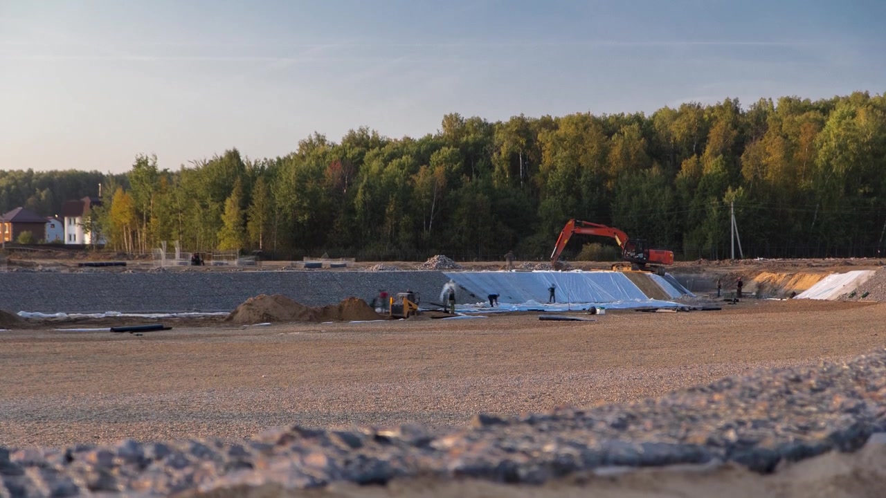 Paesaggio panoramico che si trasforma in area urbana con escavatori e bulldozer in timelapse. Veduta di un cantiere per un nuovo villaggio di villette in un ampio campo. Foresta verde e cielo blu.