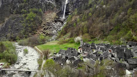 aerial flyover over the rooftops of the old stone houses in the village of foroglio towards the waterfall in the spring time alpine landscape