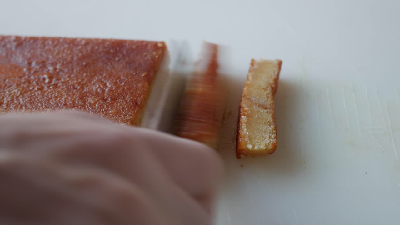 A knife slicing through a golden, crispy Toasted Egg Yolk Turron on a clean white surface