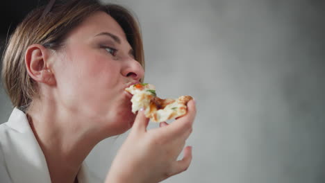 close up of lady in white outfit eating pizza slice with melted cheese and toppings, enjoying every bite with playful expression, holding pizza near mouth against cozy blurred background