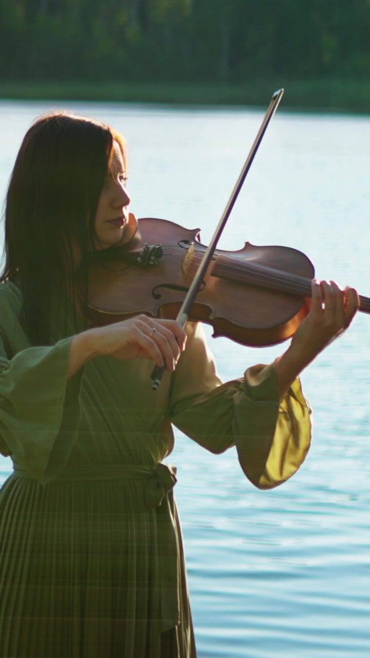 Woman Playing Violin by a Calm Lake at Sunset