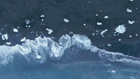 waves crashing on iceberg fragments scattered on the black sand of diamond beach in iceland