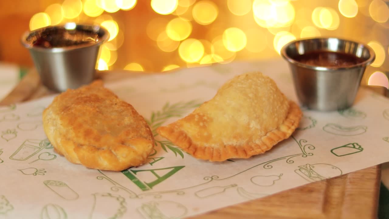 dos empanadas gourmet servidas con salsas de inmersión en una bandeja con luces borrosas en el fondo