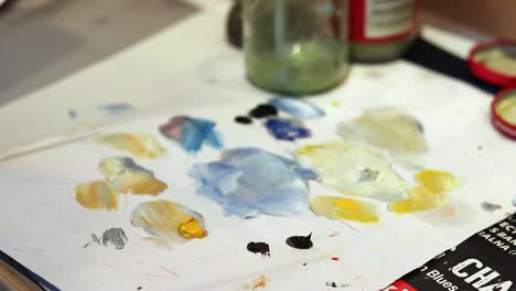 an older woman is mixing oil paints with a slim precise brush