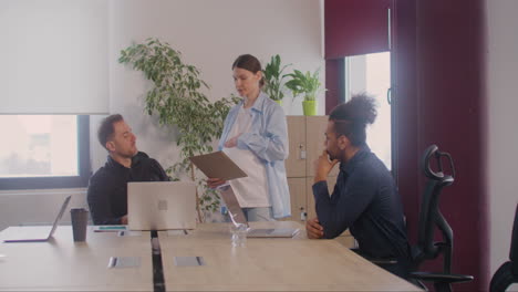 Pregnant-Woman-Is-Explaining-A-Project-To-Coworkers-In-A-Meeting-Room-While-She-Is-Touching-Her-Belly