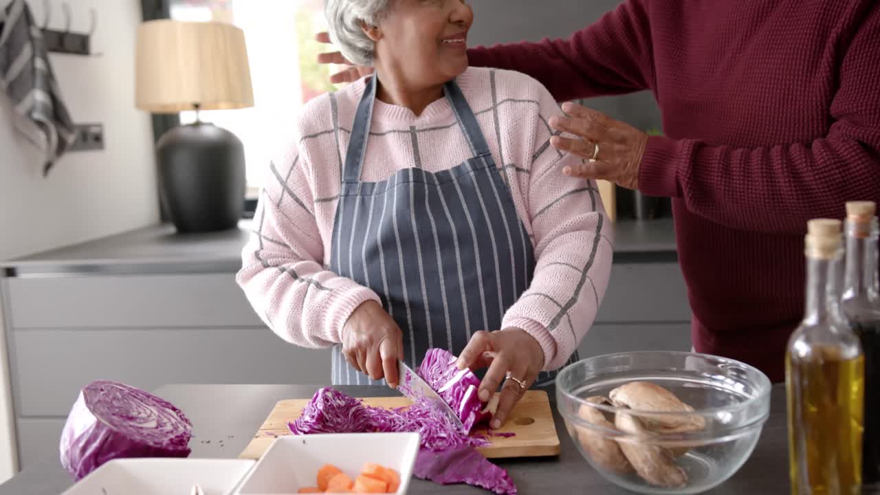 pareja biracial senior cocinando la cena y cortando verduras en la cocina, sin alterar, en cámara lenta
