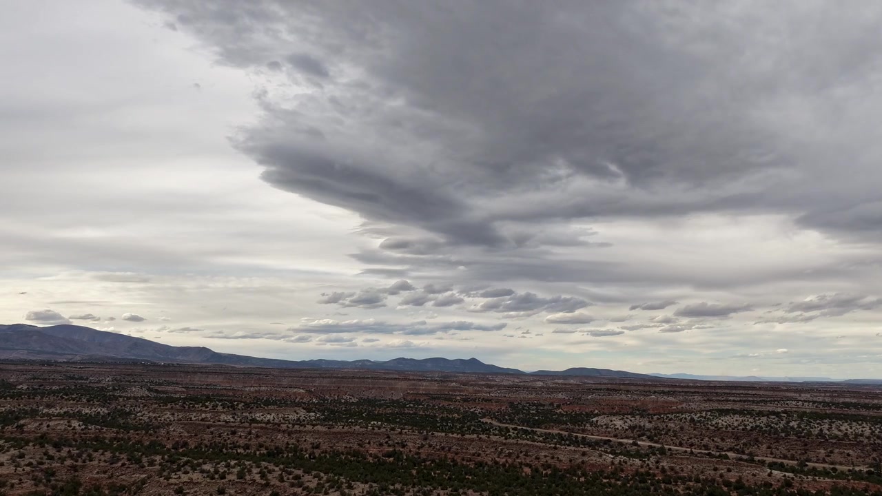 A dramatic drone timelapse features a layered cloudscape shifting over southwestern desert mesas and distant mountains. The atmospheric motion provides a professional nature transition for B-roll.