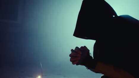 silhouette of a hooded figure in prayer