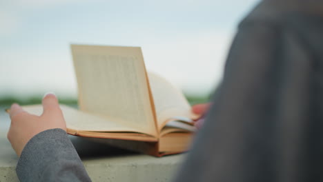 closeup back view of an individual wearing grey clothing holding an open book, as the person turn to a new page while the wind gently blows through the pages