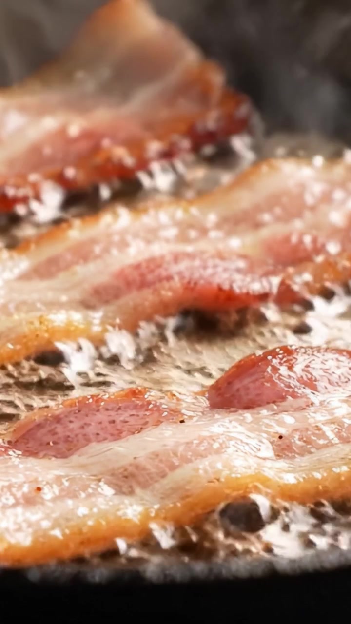 Sydende bacon steger til sprød perfektion: Et mundvandsløbende nærbillede af baconskiver, der steger på en varm pande, fanger den saftige tekstur og lækre aroma