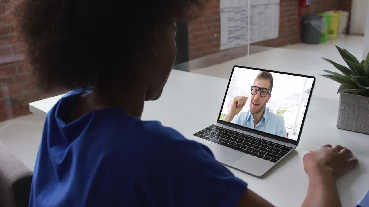 Donna d'affari afroamericana seduta alla scrivania che usa il laptop in videochiamata con un collega