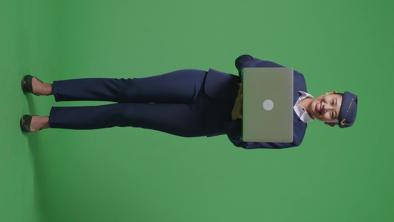 cuerpo lleno de mujer asiática azafata sonriendo y señalando a una computadora portátil en su mano mientras estaba de pie en el estudio de fondo de la pantalla verde