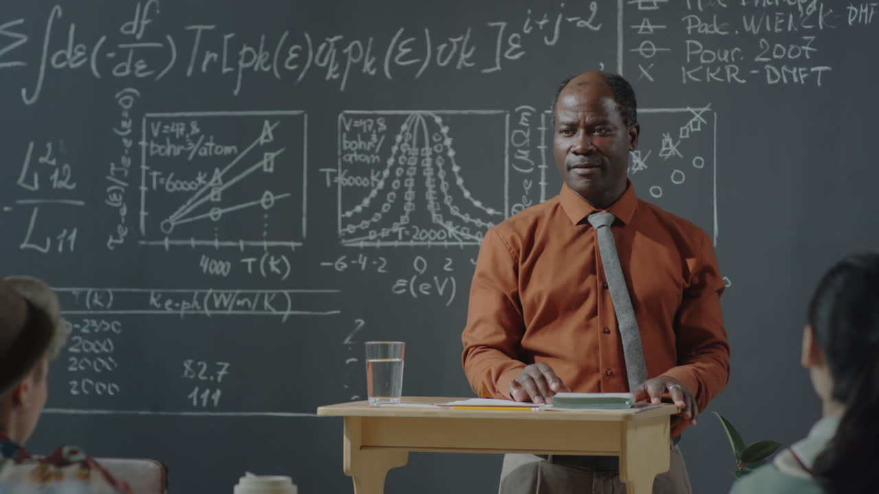 Professore afroamericano che tiene una lezione in un'aula con formule scientifiche su una lavagna.