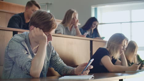 Un-Gran-Grupo-De-Hombres-Y-Mujeres-Se-Sientan-En-El-Auditorio-De-La-Universidad-Y-Miran-Vídeos-En-Internet-En-Teléfonos-Inteligentes,-Escriben-Mensajes-Y-Chatean-En-Línea.-Comportamiento-Antisocial-De-Los-Introvertidos.-El-Problema-Moderno-De-La-Sociedad.