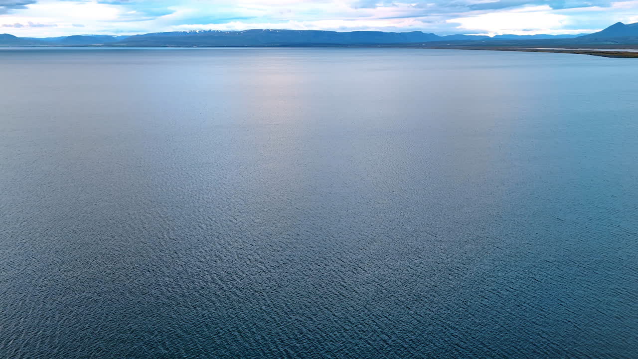 Vast peaceful waterscape limited by the silhouette of mountain range. Stunning nature of Iceland from drone.