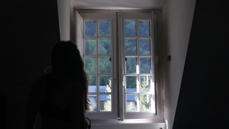 splendida ripresa al rallentatore in condizioni di scarsa luminosità di una giovane donna caucasica che apre una finestra su uno scenario naturale in francia