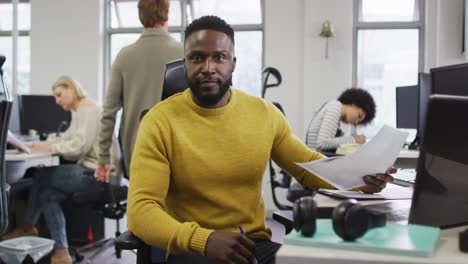 Portrait-of-smiling-african-american-creative-businessman-sitting-by-desk-in-modern-office