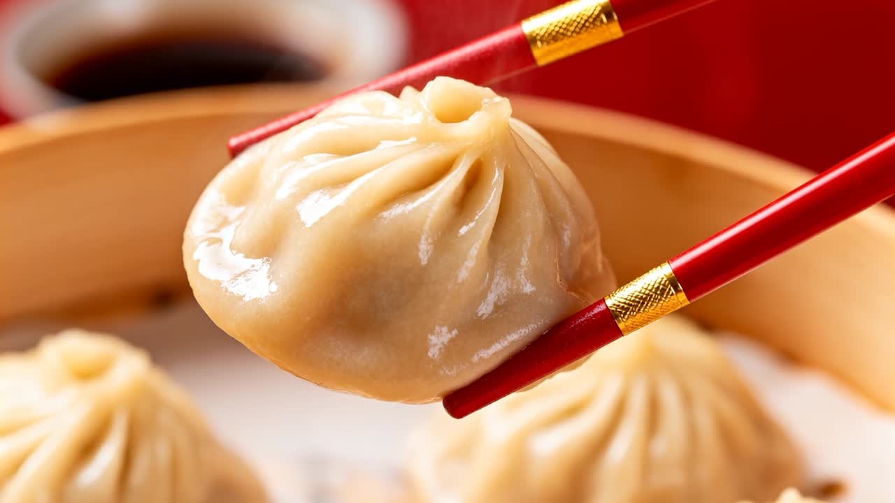 Genggaman yang erat, sumpit merah mengangkat xiao long bao dari pengukus bambu di meja, menawarkan lipatan