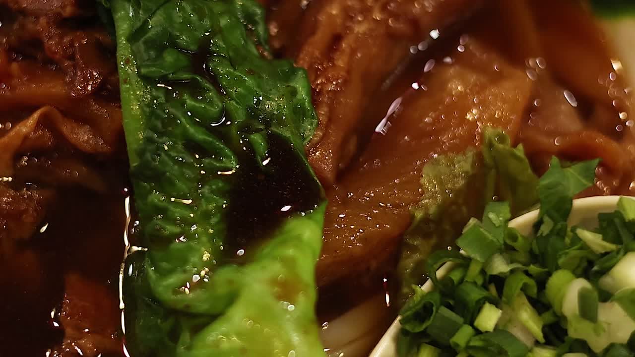 A detailed view of a noodle dish featuring vibrant greens and rich broth.