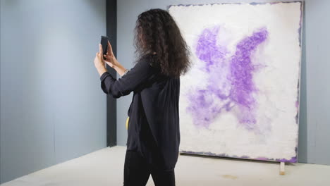 mujer tomando una foto de pinturas abstractas en una galería de arte