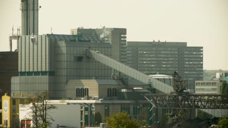 industrial area featuring modern buildings, conveyors, and a mining crane in the foreground, sunny day