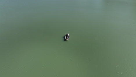 aerial view circling tiny fishing boat floating on shimmering sunlit emerald green water