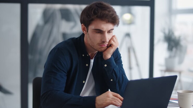 Nahaufnahme eines gelangweilten Geschäftsmannes, der im Büro auf den Computerbildschirm blickt.