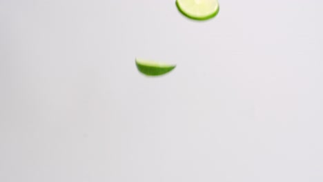 Green-lime-wedges-and-slices-raining-down-on-white-backdrop-in-slow-motion