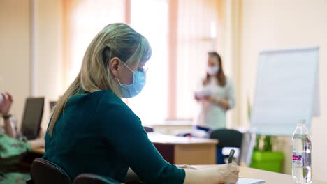 woman wearing glasses and mask writing down. female student taking notes of a lecture at university.