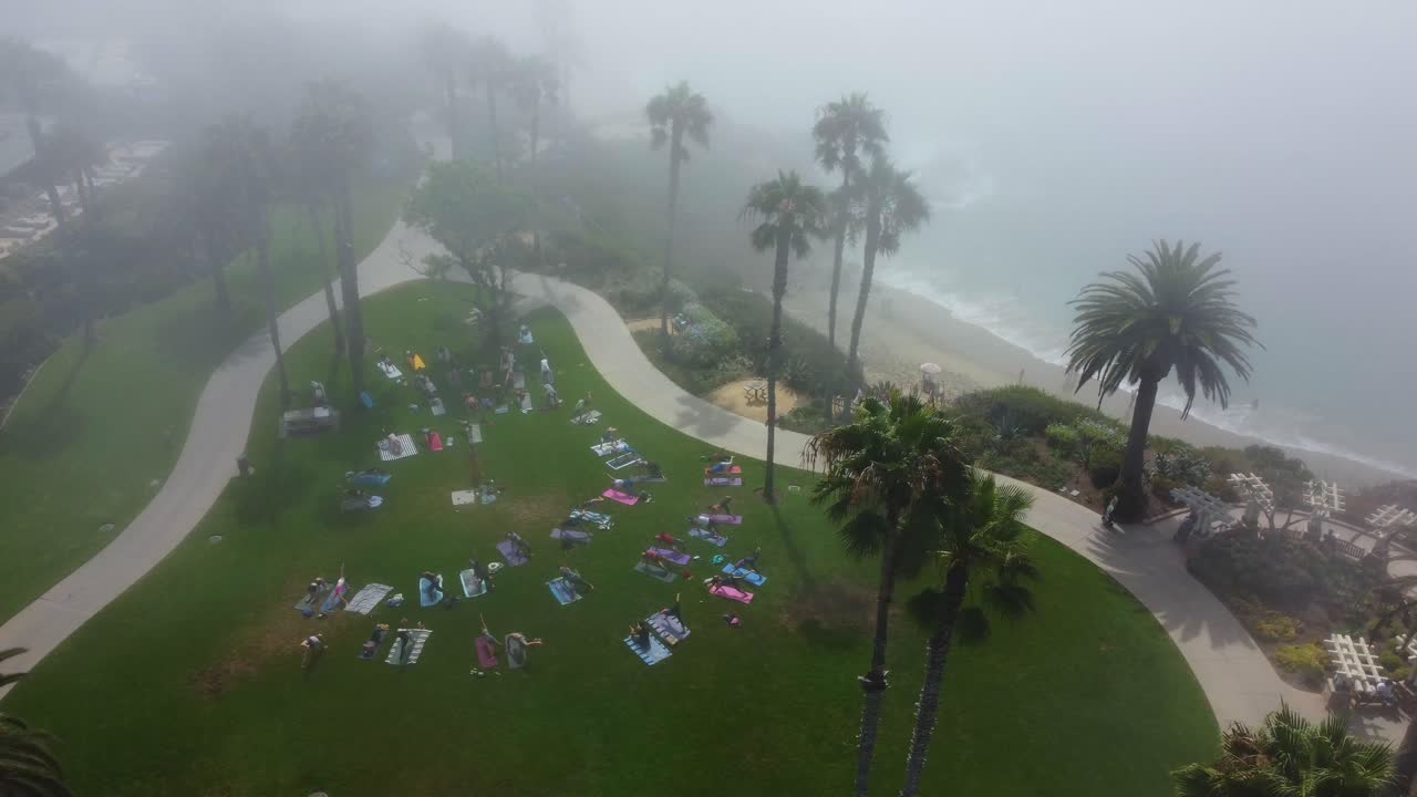 안개 속에서 아침 운동을 하는 해변가 공원 잔디에 있는 사람들의 조감도, 드론 샷
