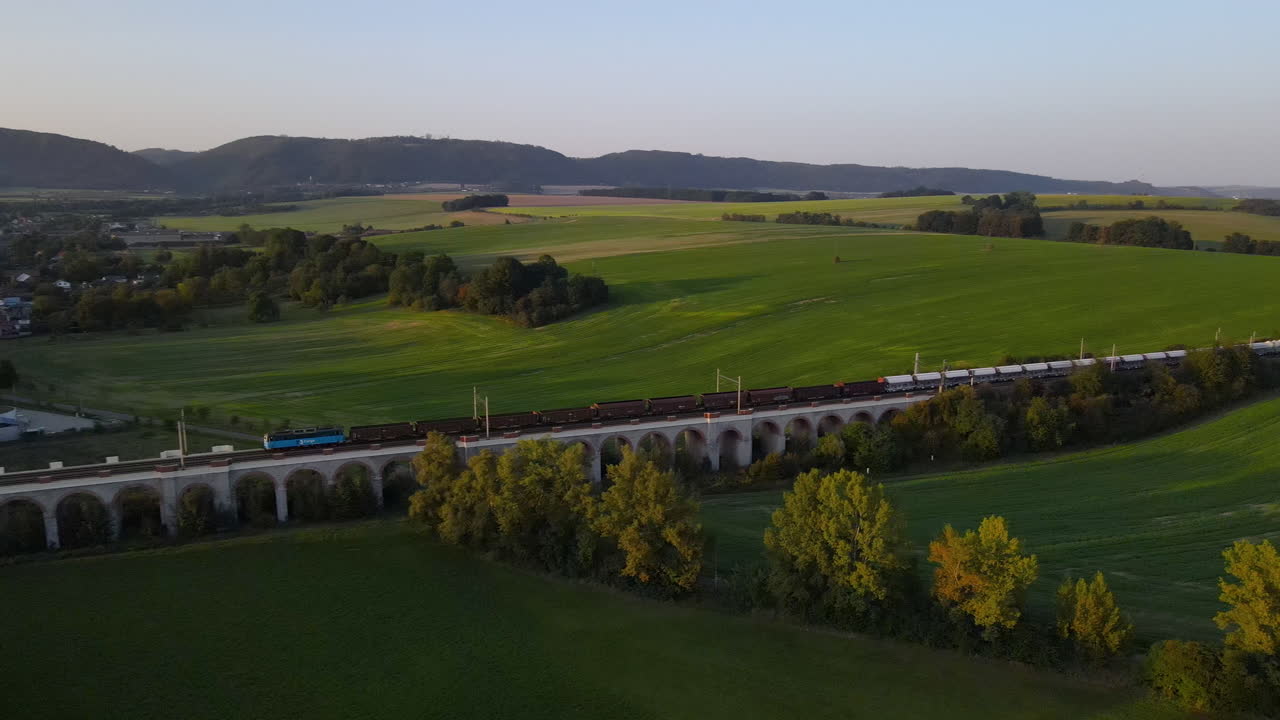 vista aérea de un viaducto de tren con un tren que pasa y el campo y la ciudad circundantes en el fondo
