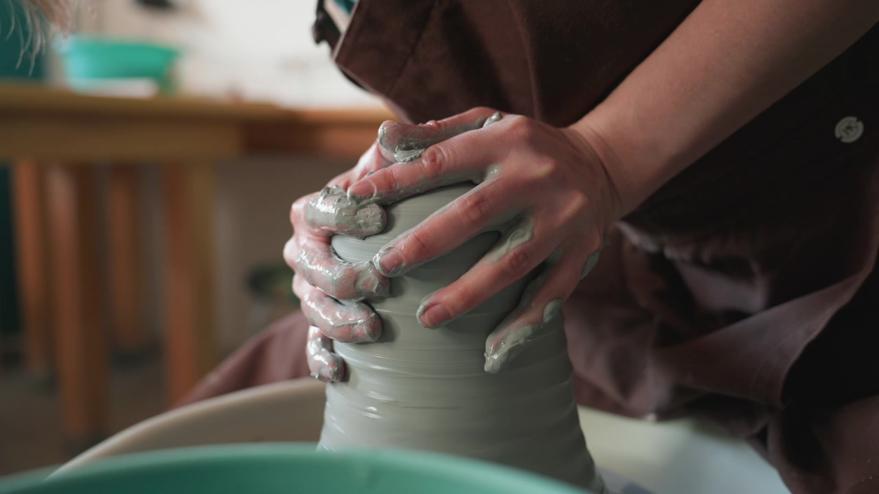 Processo di creazione della ceramica. Gruppo di artigiani che modellano un alto vaso di ceramica al tornio sotto la luce del sole. Ambiente di laboratorio dove gli artigiani creano collaborativamente un alto vaso con il supporto dell'istruttore.