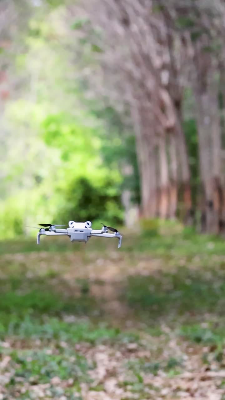Un drone bianco compatto si libra all'altezza degli occhi attraverso un sentiero panoramico alberato in Thailandia.