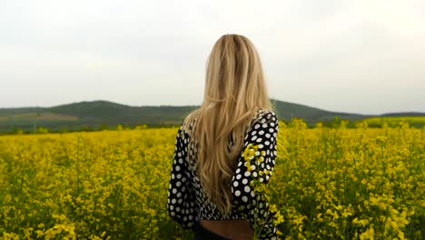 blond woman walking in field of yellow rapeseed, handheld slow motion