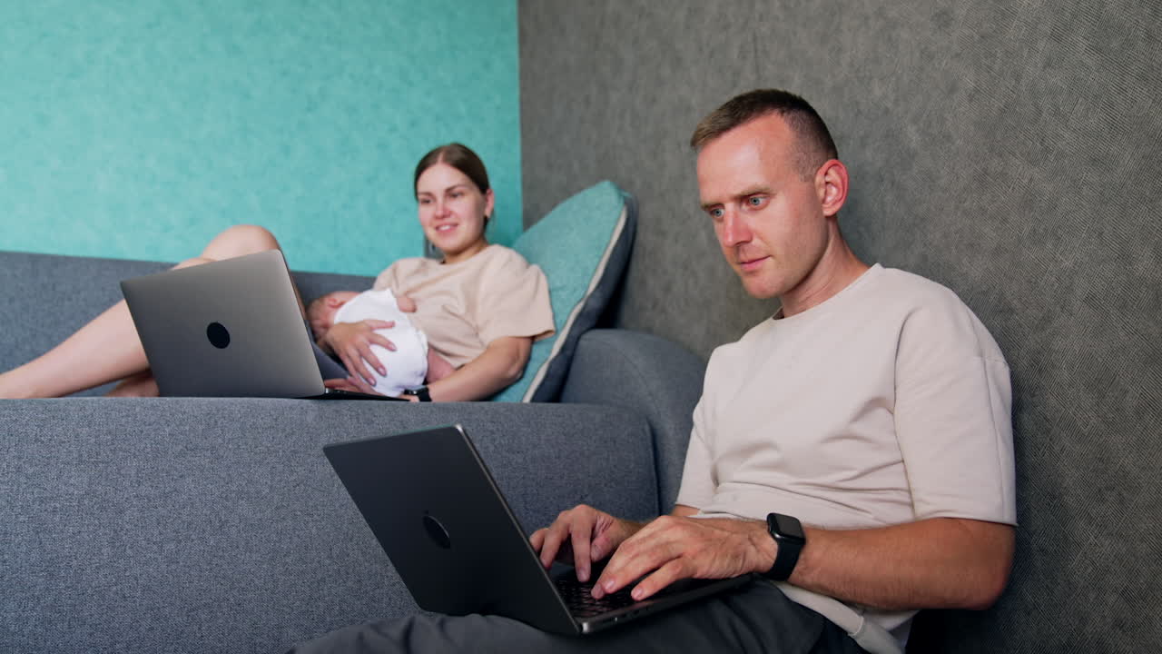 Positive Caucasian people having laptops and work remote. Woman has a sleeping newborn in hands and looks at her computer. Low angle view.