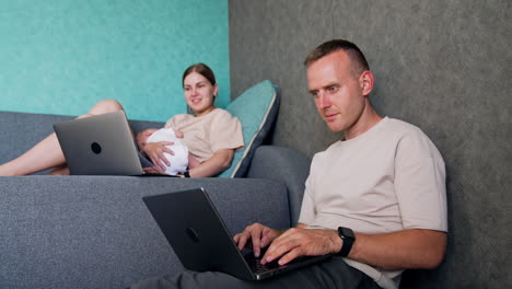 positive caucasian people having laptops and work remote. woman has a sleeping newborn in hands and looks at her computer. low angle view.