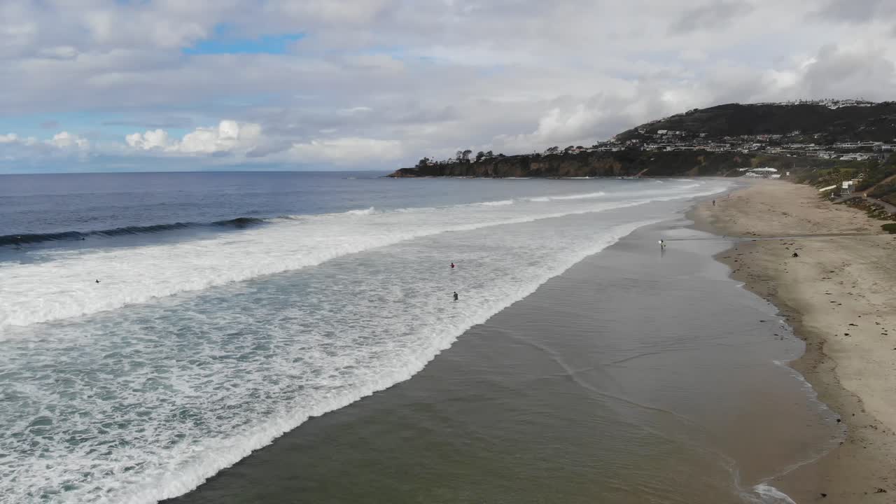 un dron vuela sobre las olas del océano en la playa mientras los surfistas reman para surfear