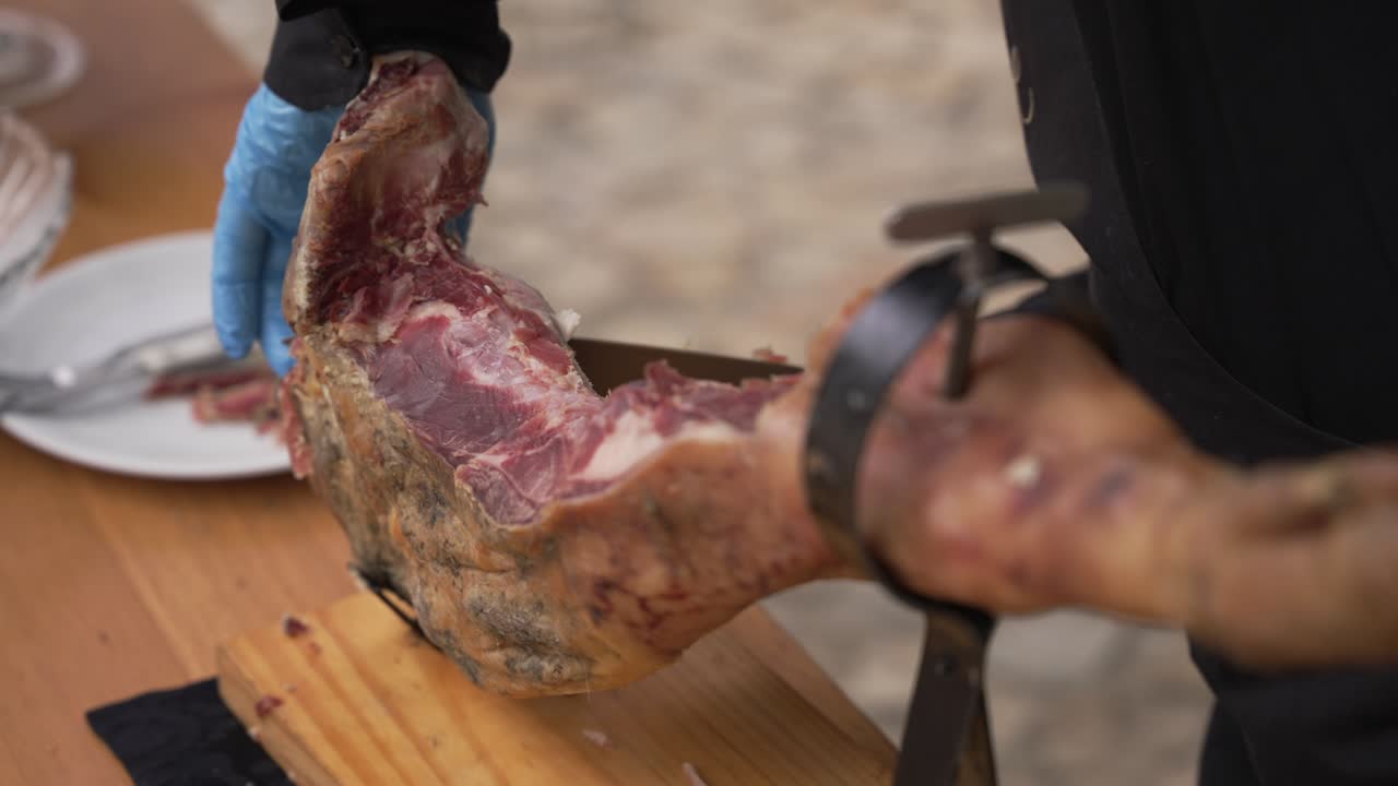 dry cured ham leg being sliced on wooden table with gloves outdoors