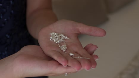 la novia con un delicado collar de perlas en sus manos durante los preparativos de la boda