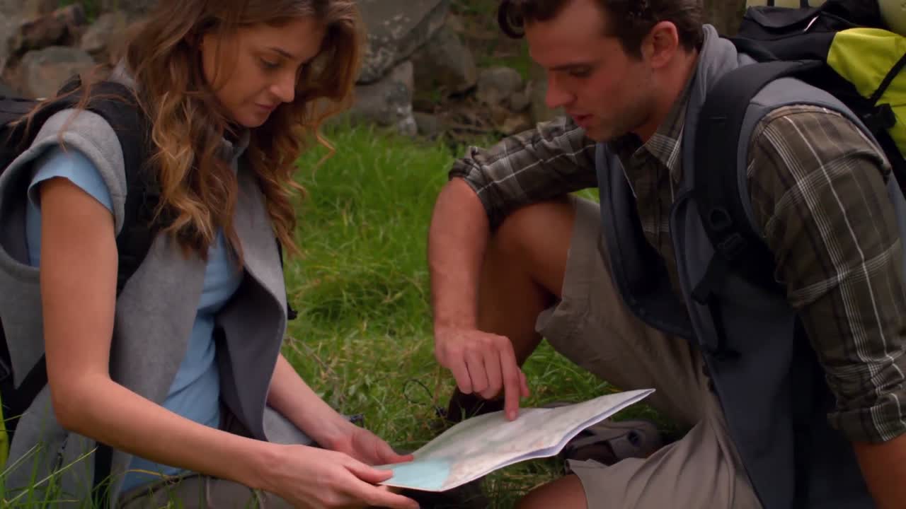 pareja sonriente con un mapa en una caminata en el campo