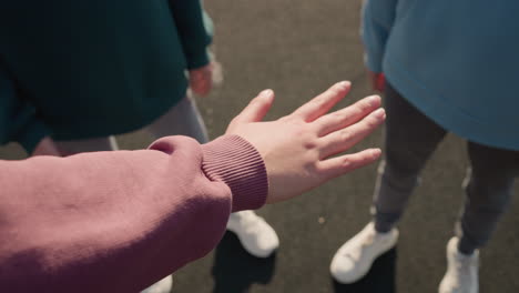 close-up of hand stretched out with other people in background placing their hands together as team in sports activity, showing unity, collaboration, and teamwork in outdoor setting