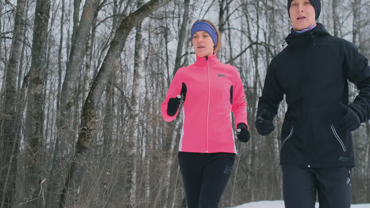 Young family couple man and woman on a morning jog in the winter forest. A woman in a loose jacket a man in a black jacket is running through a winter park. Healthy lifestyle happy family