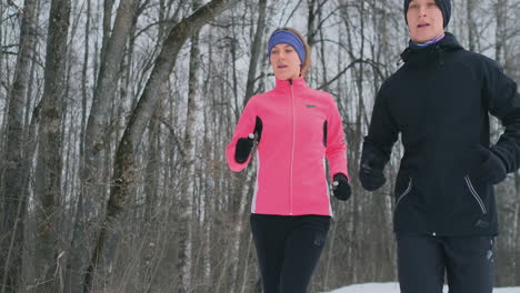 joven pareja familiar, hombre y mujer, corriendo por la mañana en el bosque de invierno. una mujer con una chaqueta holgada y un hombre con una chaqueta negra corre por un parque de invierno. estilo de vida saludable familia feliz