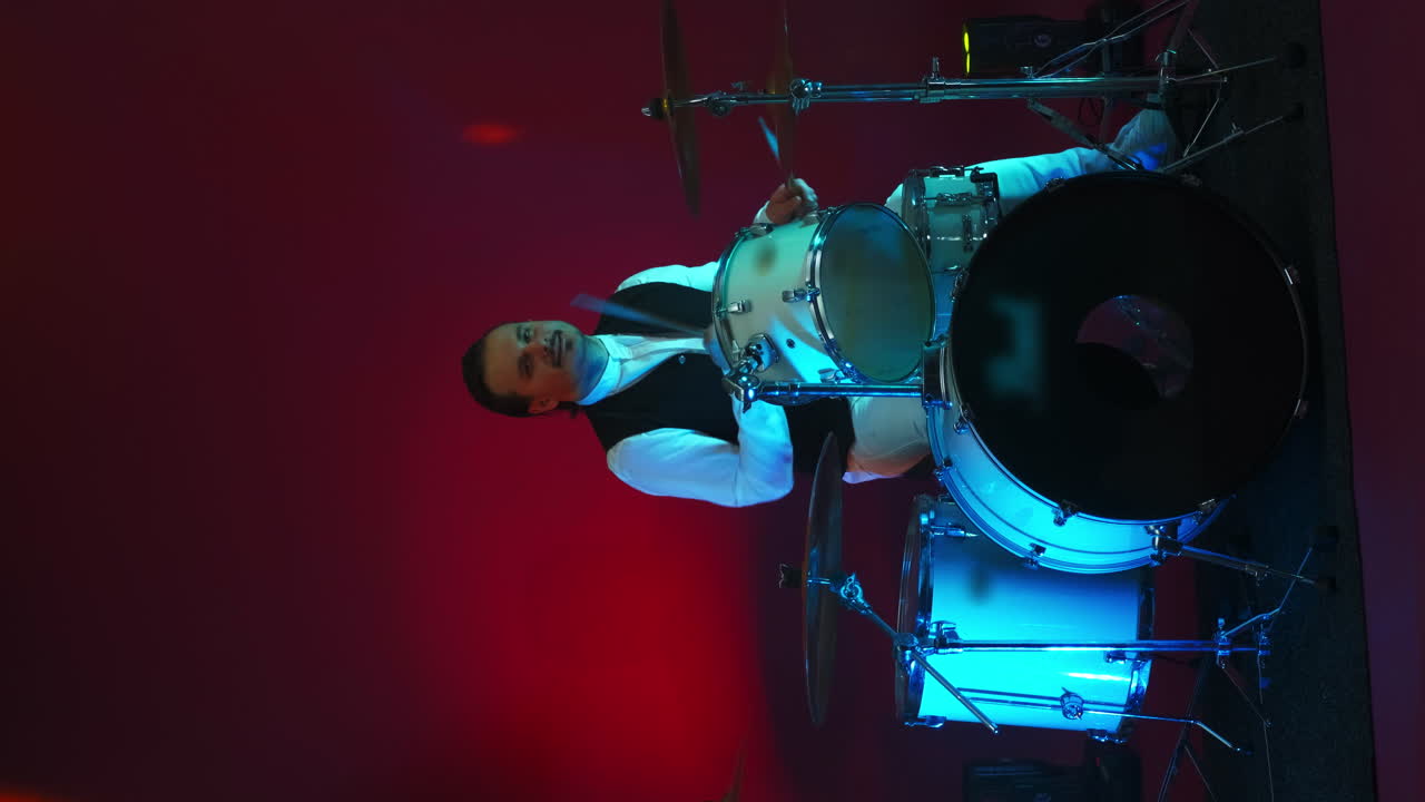 Un uomo che suona la batteria su un palco cupo. Illuminazione al neon. Video verticale.