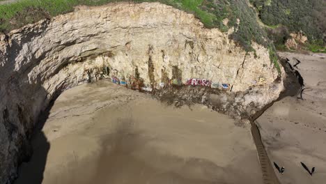 Aerial-view-of-Graffiti-on-rocks-as-waves-crash-on-floor,-Daven-port-Shark-Fin-Cove,-Highway-1-California