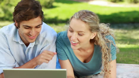 mujer se acuesta al lado de su novio mientras miran una computadora portátil y luego miran a la cámara