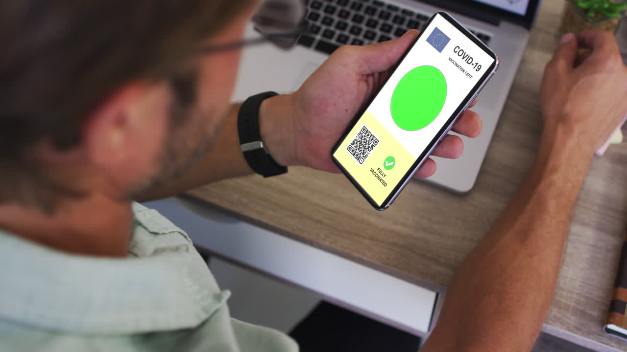 hombre en el escritorio con un teléfono inteligente con certificado de vacunación contra la covid, bandera de la ue y código qr en la pantalla