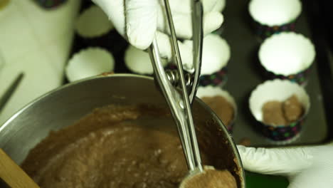 Filling-cupcake-pans-with-chocolate-batter,-using-an-ice-cream-spoon