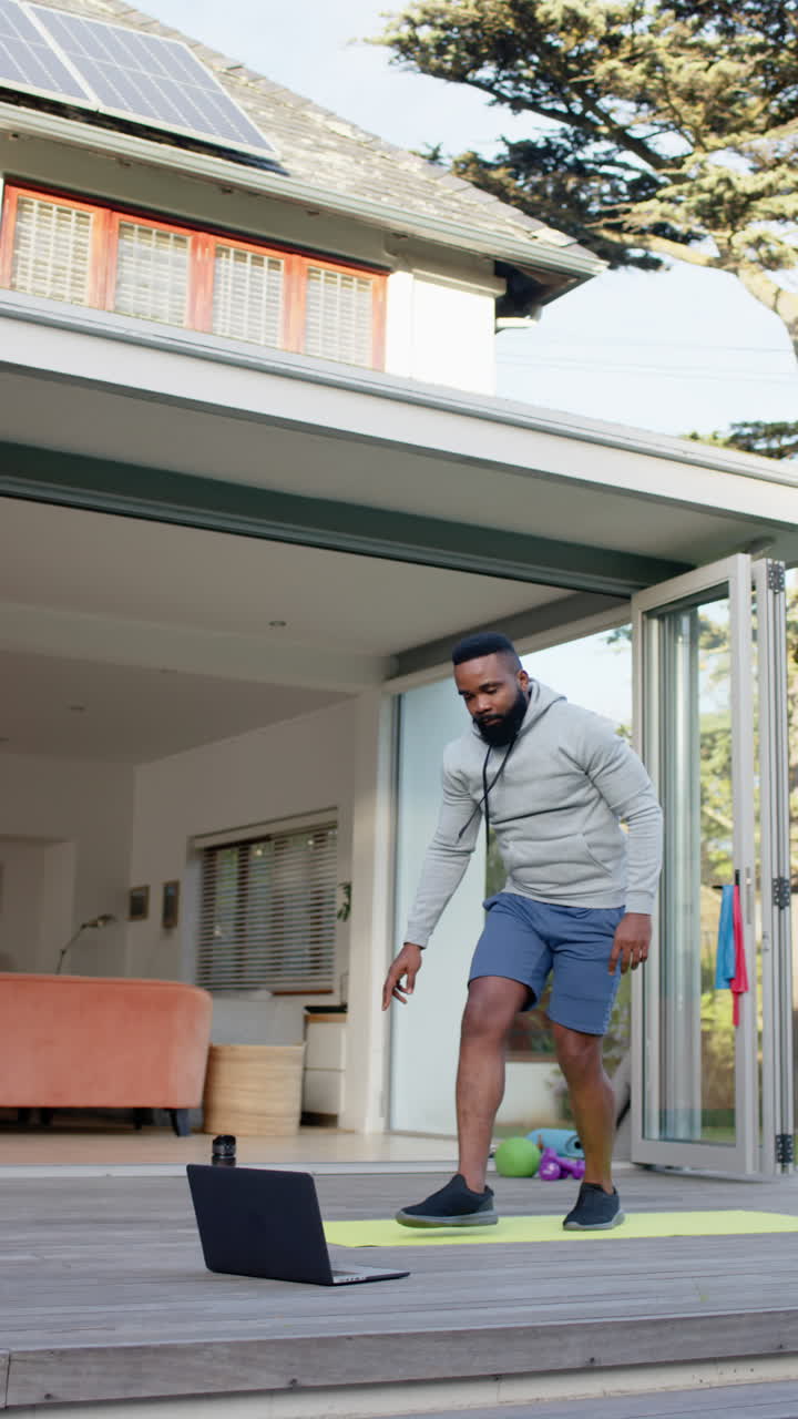 Vertical video of african american man fitness training exercising on deck in garden, slow motion